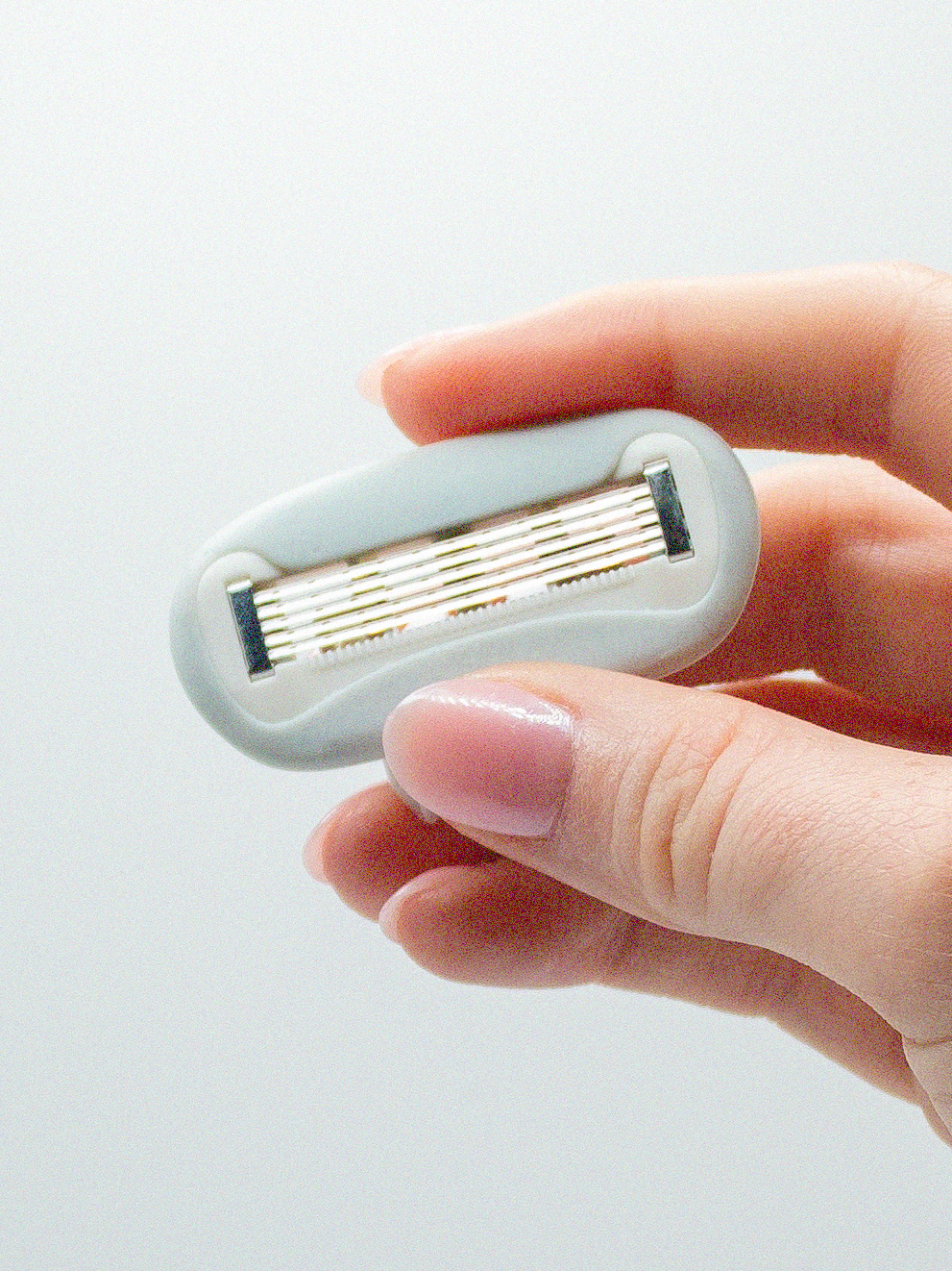 Razor blade cartridge held in a hand against a light gray background