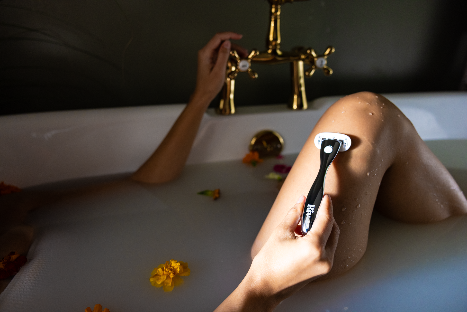 Person shaving leg with a razor in a bathtub filled with flowers