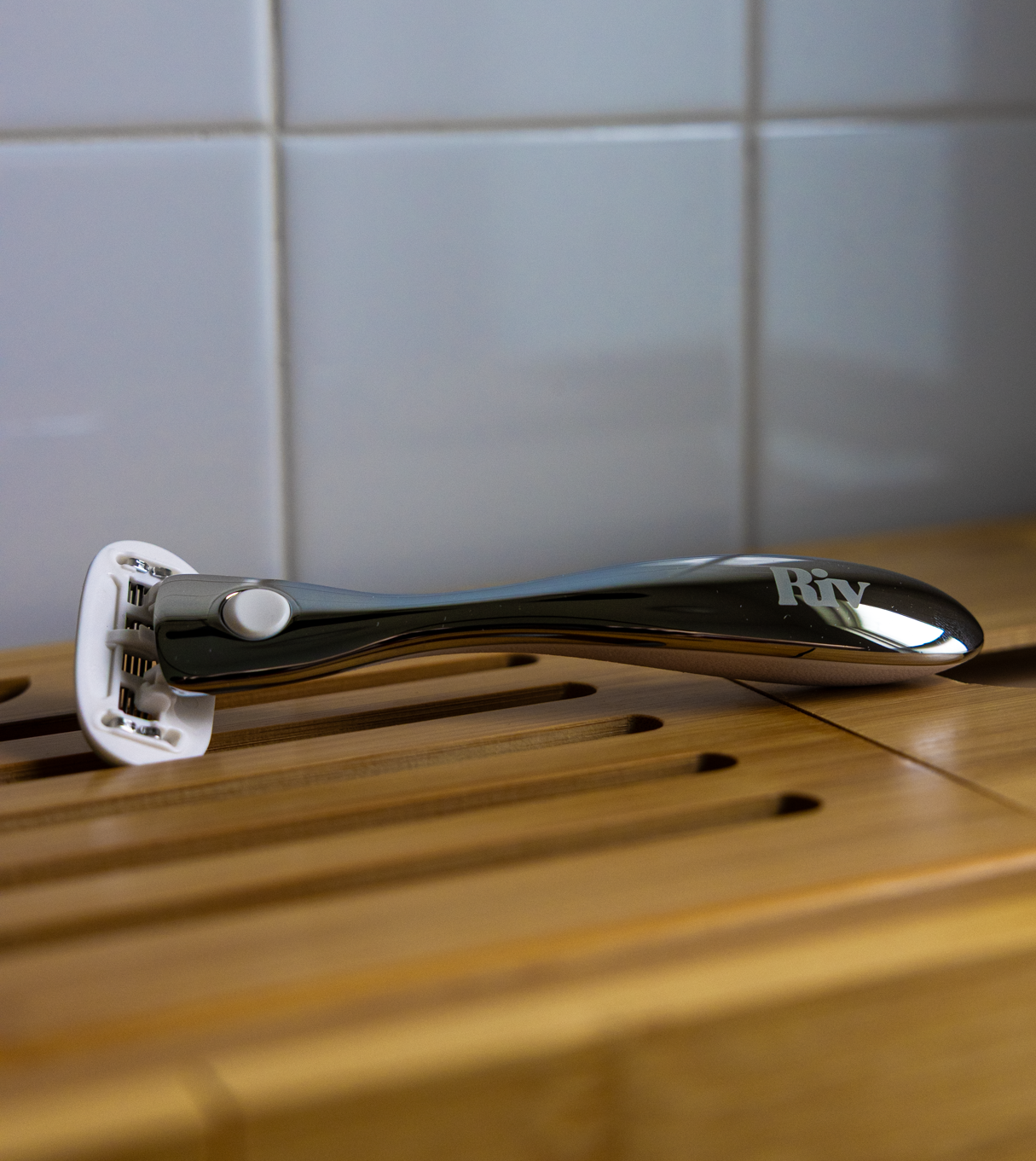 Metallic razor on wooden cabinet tabletop with tiled bathroom